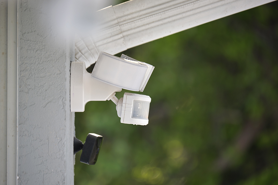 Motion sensor with light detector mounted on exterior wall of private house as part of security system.